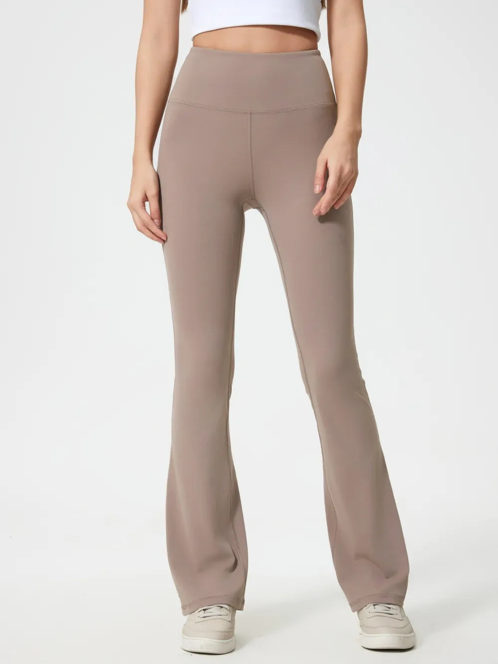 A model stands in taupe high-waist active pants with a smooth fitted silhouette, curved waistband seam, and gently flared legs.