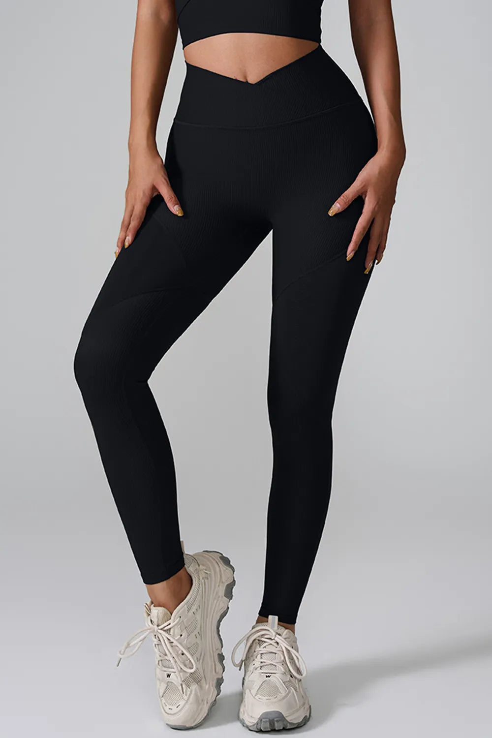 A model poses in black high-waist active leggings with a fitted full-length silhouette, subtle ribbed texture, curved seam panels, and one knee bent.