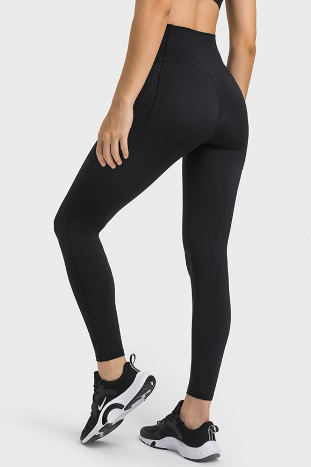 Model poses in black V-waist yoga leggings with side pockets, a high-rise waistband, seam detailing, and a sleek full-length fitted silhouette.