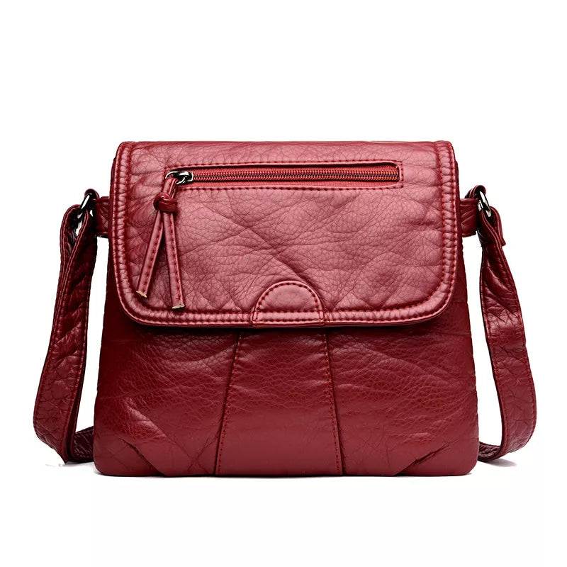 Small burgundy PU leather crossbody bag with an adjustable strap, flap closure, front zip pocket, and softly structured stitched construction.