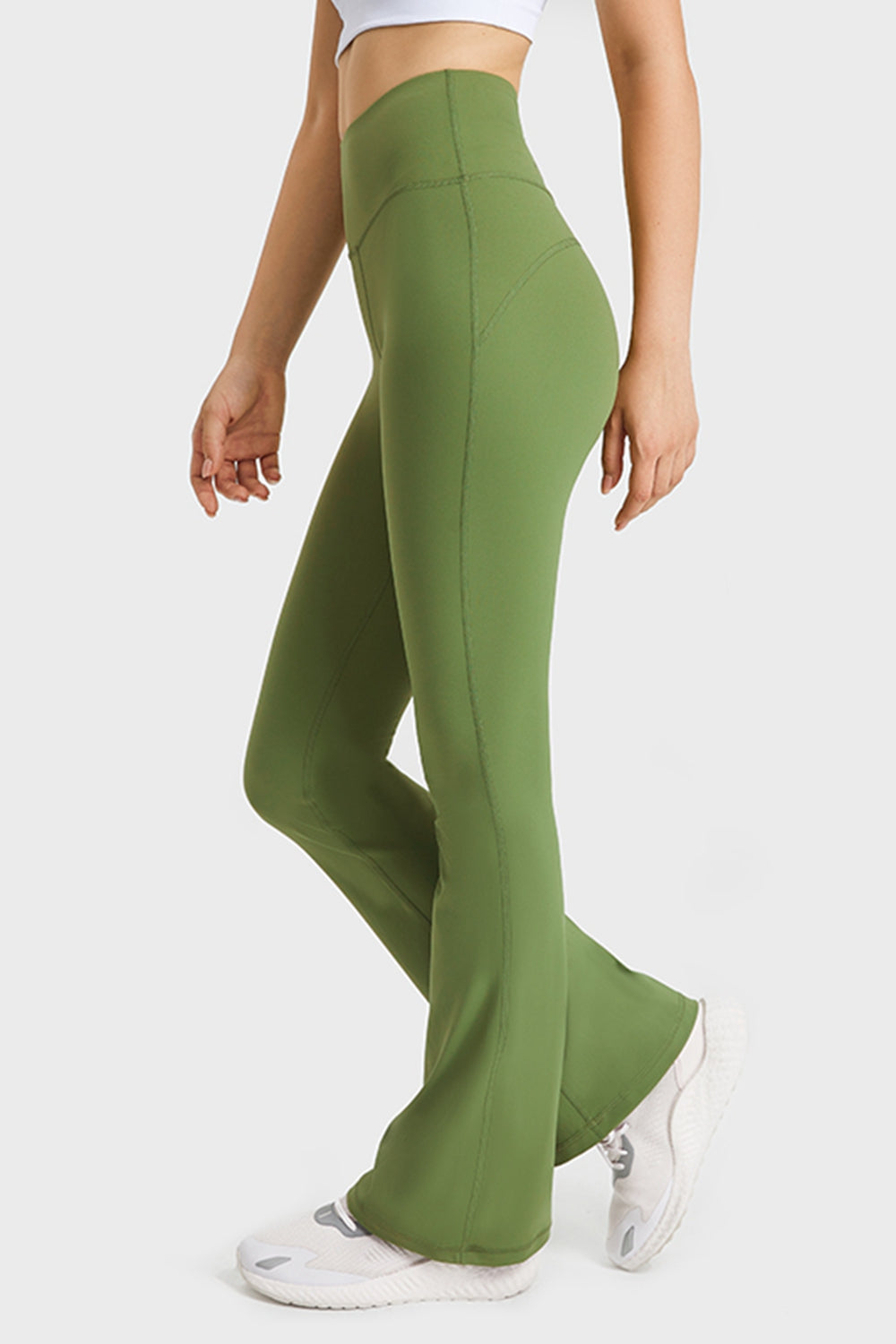 A model poses in olive green high-waisted flare yoga pants with a smooth stretch fit, long silhouette, and visible curved seam detailing.