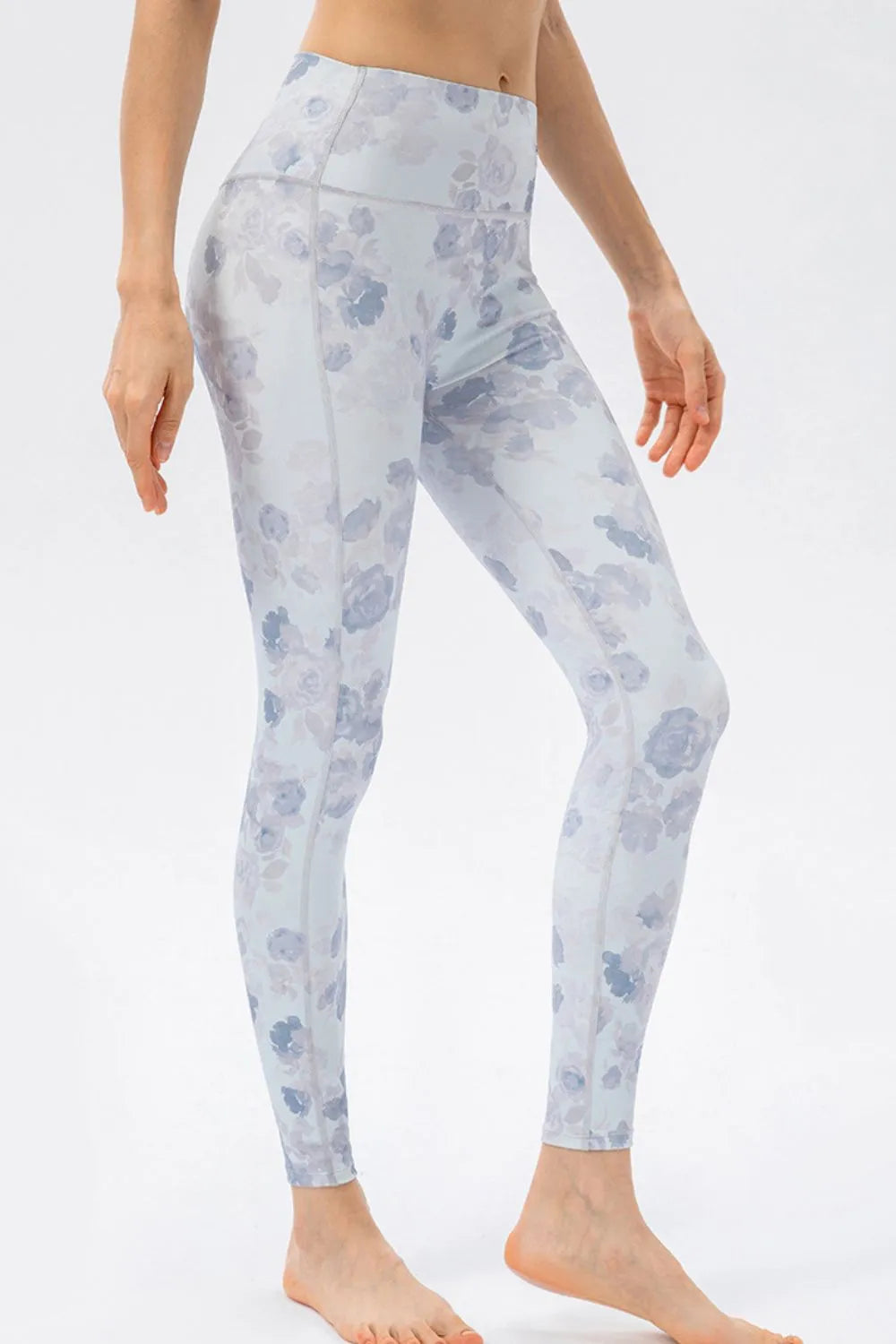 Model poses in high-waist skinny active leggings with a pale blue and gray floral print, fitted silhouette, stretch fabric, and visible seam construction.
