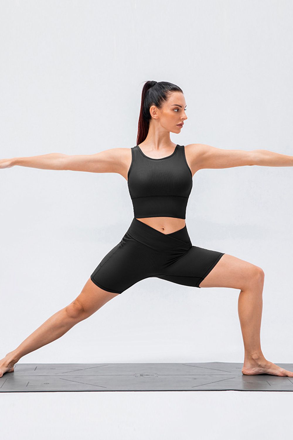 A model holds a wide lunge in black slim-fit sports shorts with a high V-shaped waistband and fitted mid-thigh silhouette.