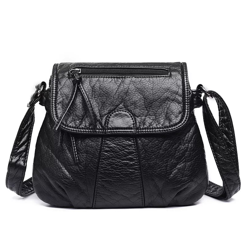 Small black PU leather crossbody bag with an adjustable strap, textured finish, stitched panel construction, flap closure, and front zip pocket.