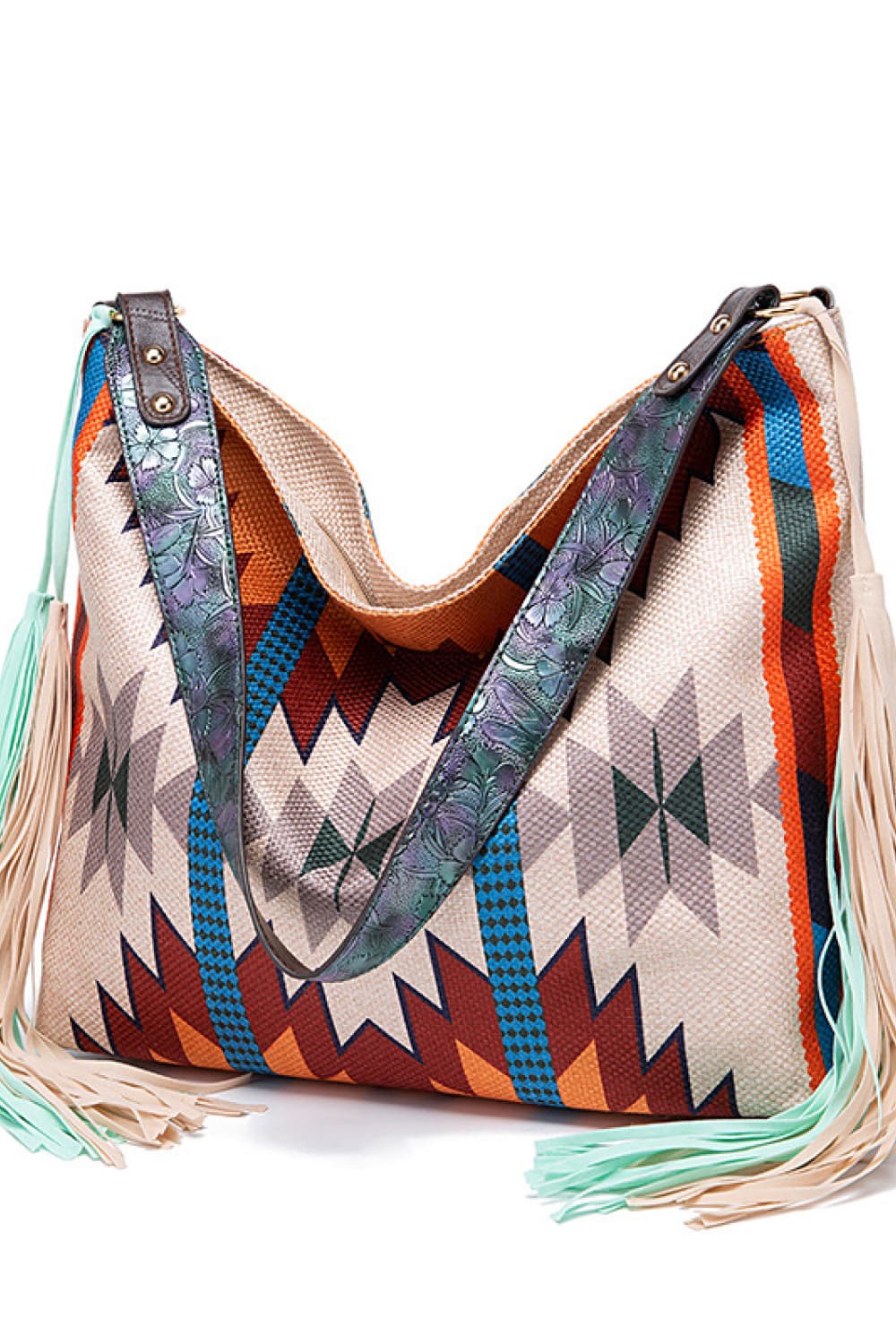 Oversized geometric canvas tote bag in cream with colorful zigzag and diamond patterns, wide decorative shoulder straps, and long fringe trim.