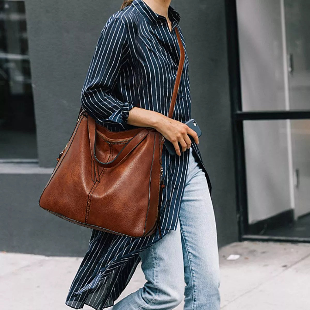 Model carries a medium brown PU leather crossbody bag with a slouchy silhouette, long adjustable strap, stitched construction, and front pouch detail.