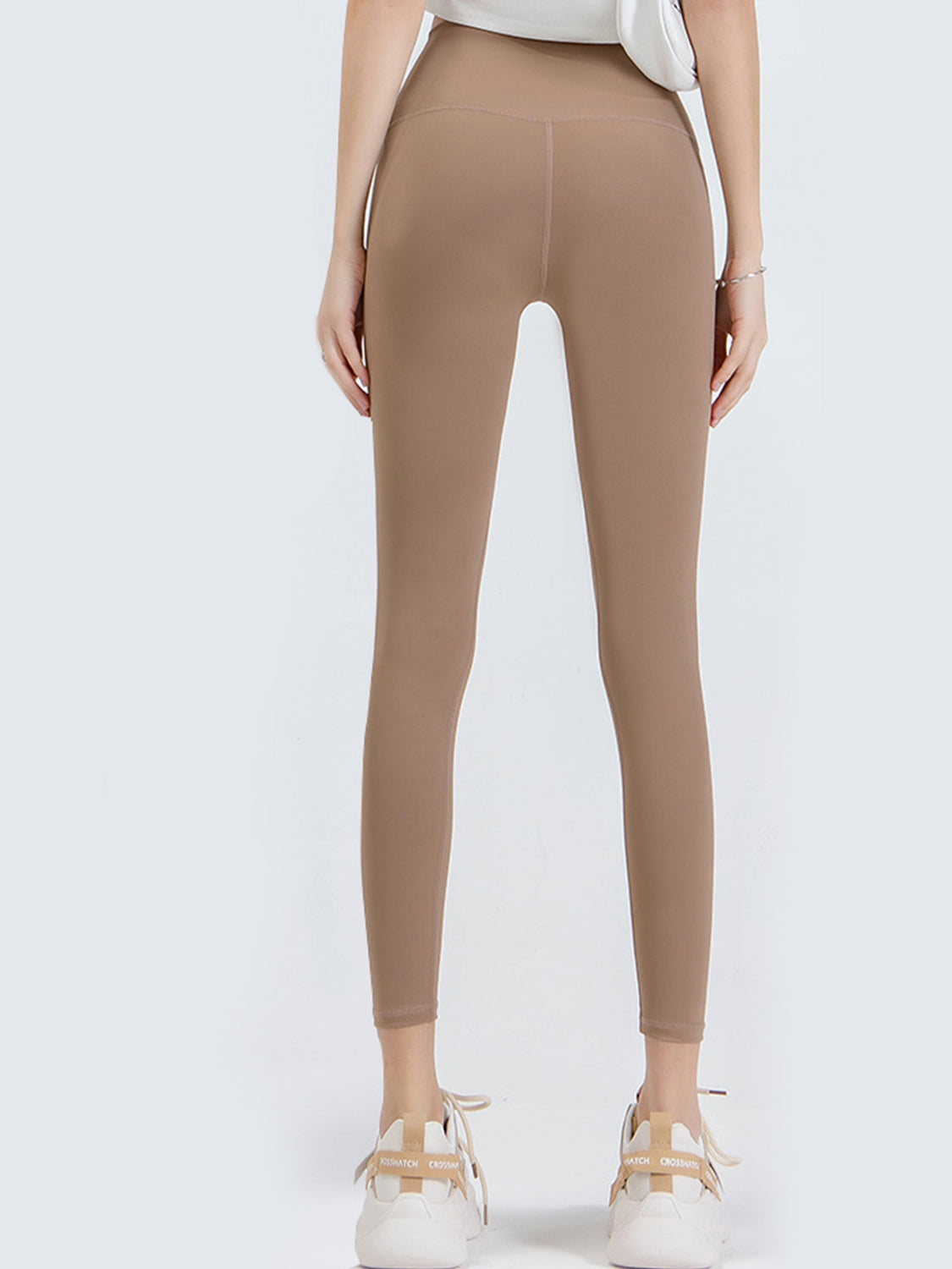 Back view of a model standing in tan wide-waistband sports leggings with a smooth, fitted full-length silhouette and visible center-back seam.