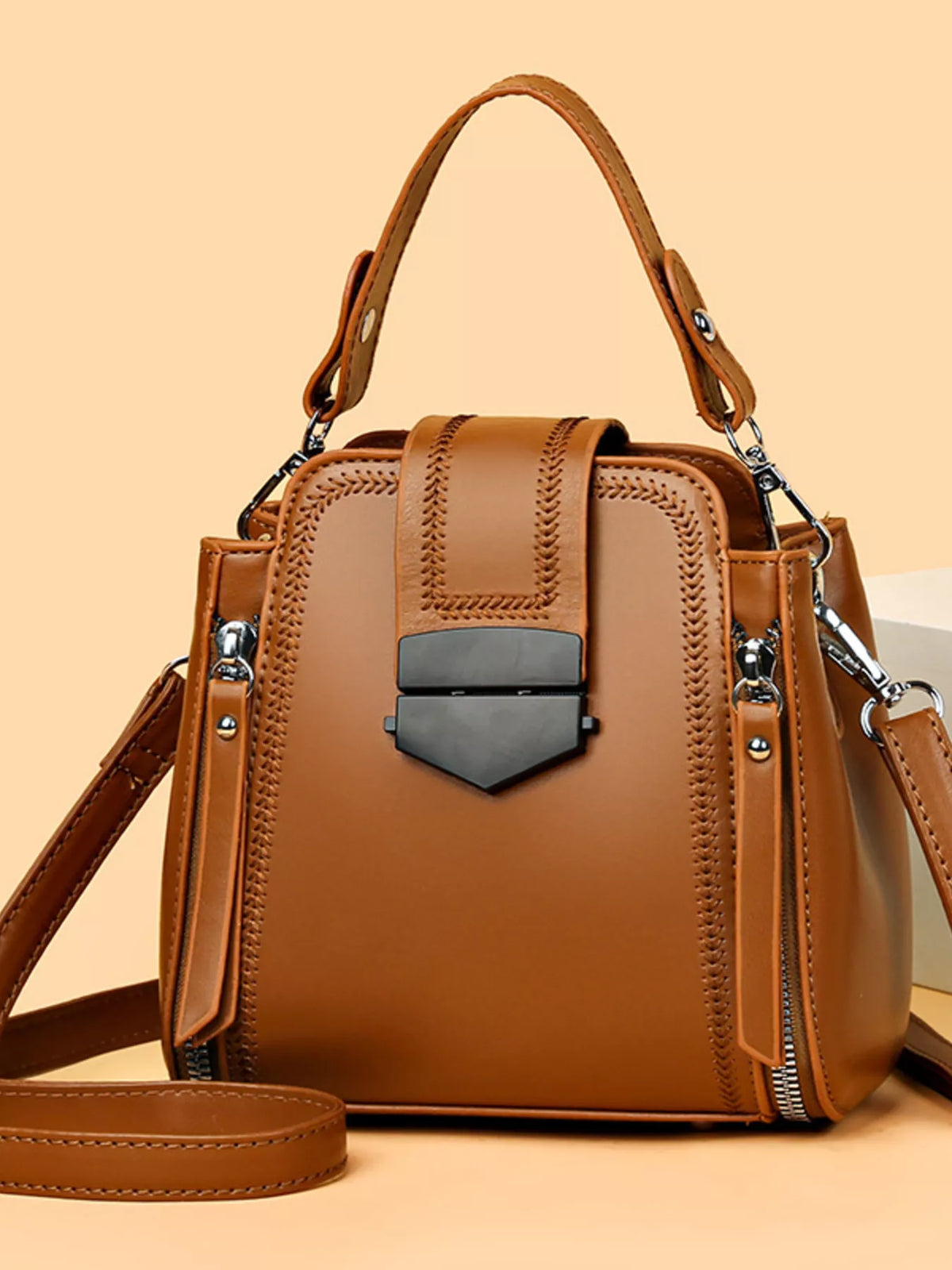 A medium brown PU leather bucket crossbody bag with a structured silhouette, top handle, detachable strap, woven stitching, and front flap clasp.