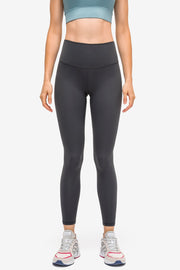 Model stands facing forward in black high-rise sports leggings with a slim, full-length silhouette, smooth matte fabric, and a wide contoured waistband.