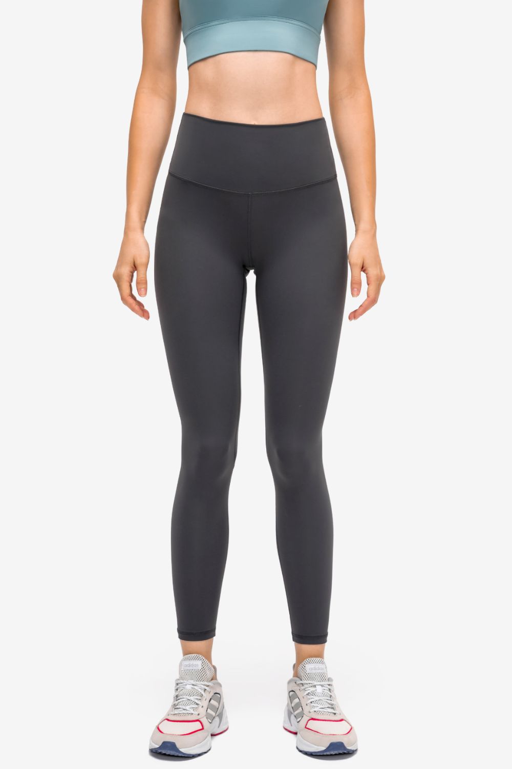 Model stands facing forward in black high-rise sports leggings with a slim, full-length silhouette, smooth matte fabric, and a wide contoured waistband.
