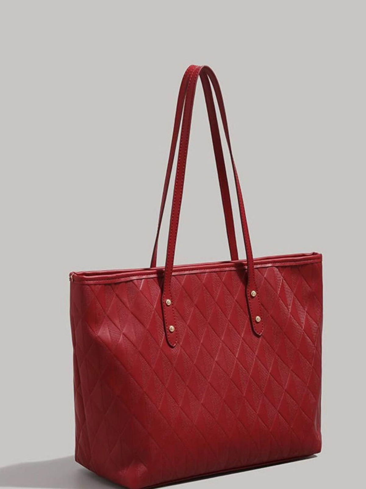 Large red textured PU leather tote bag with a quilted diamond pattern, structured silhouette, twin shoulder straps, and stitched strap attachments with metal studs.