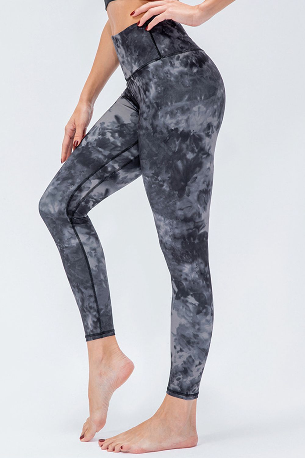 Model poses in gray and black printed active leggings with a wide waistband, slim-fit silhouette, full-length legs, and visible seam construction.
