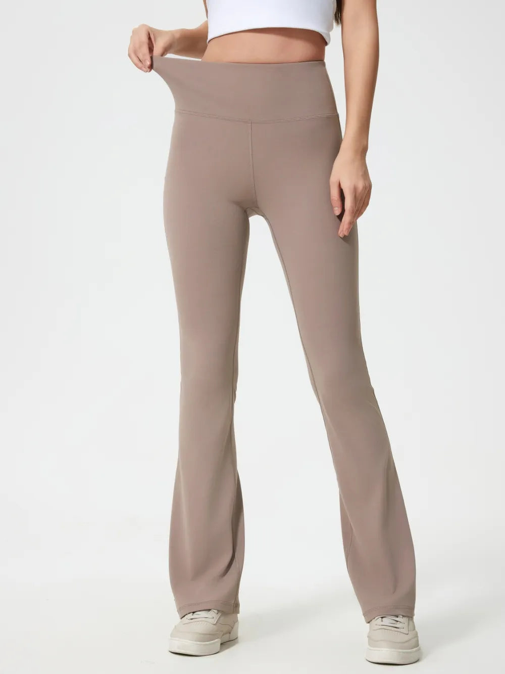 Model wears taupe high waist active pants with a wide supportive waistband, smooth stretch construction, fitted hips and thighs, and gently flared legs.