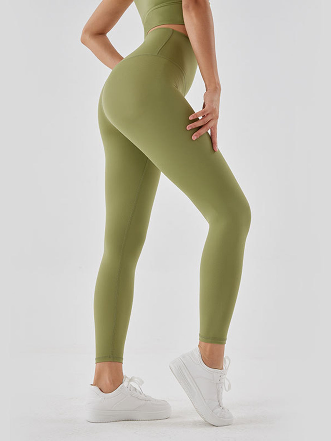 Model poses in olive green wide waistband sports leggings with a high-rise, full-length fitted silhouette and visible seam construction.