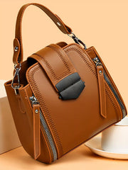 Medium brown PU leather crossbody bag with a structured silhouette, adjustable strap, stitched panels, front buckle detail, and multiple zippered compartments.