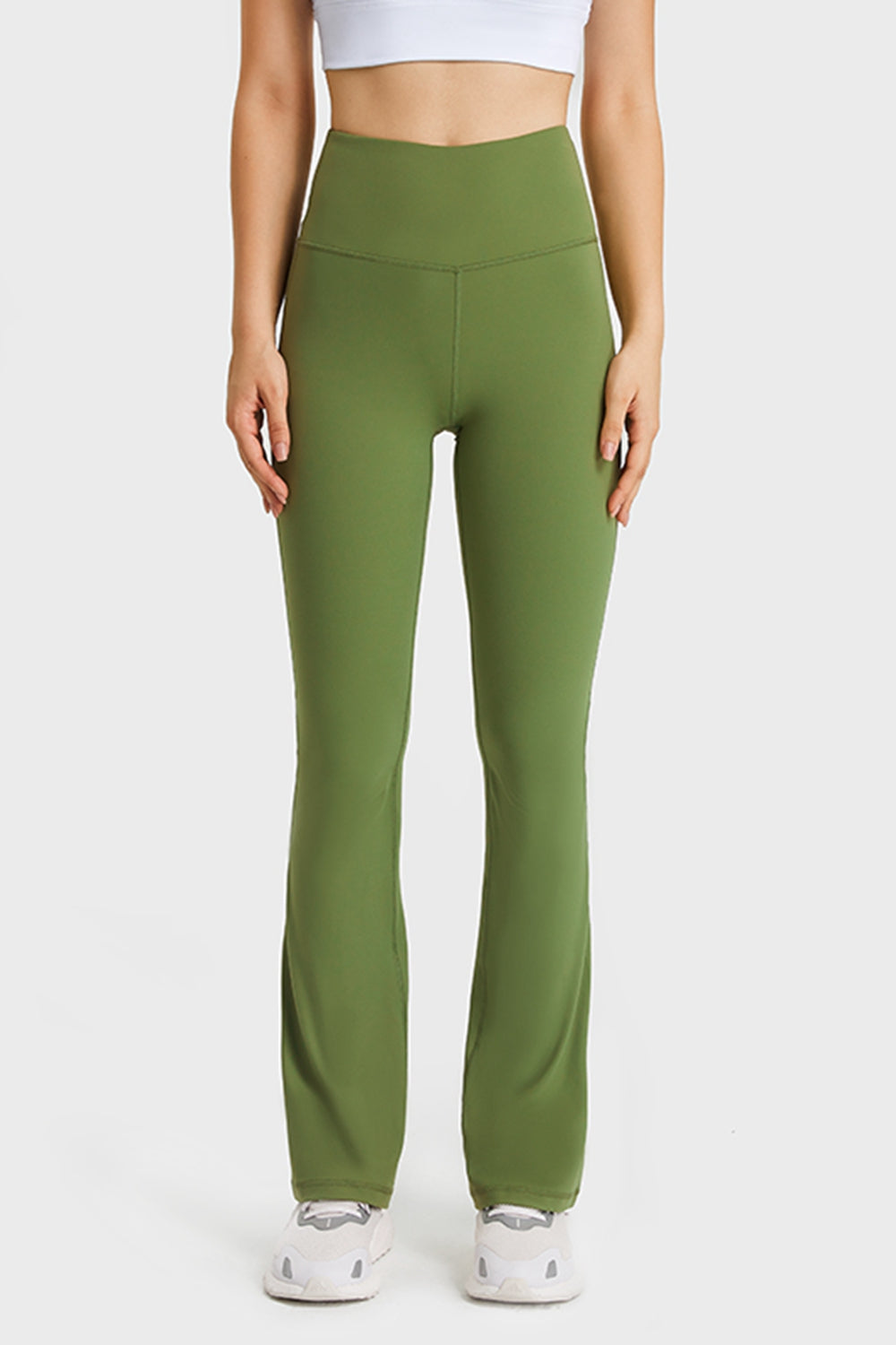 A model stands in olive green elastic-waist flare yoga pants with a high-rise fit, smooth stretch fabric, seam detailing, and long fitted-to-flared legs.