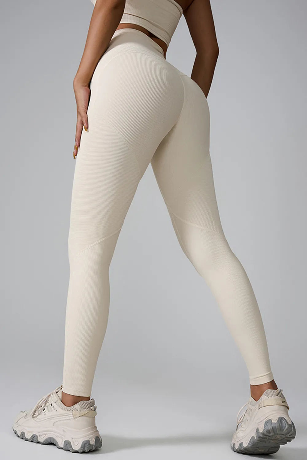 Model poses with legs apart, showcasing high-waist active leggings in cream with a ribbed texture, fitted full-length silhouette, and curved seam detailing.