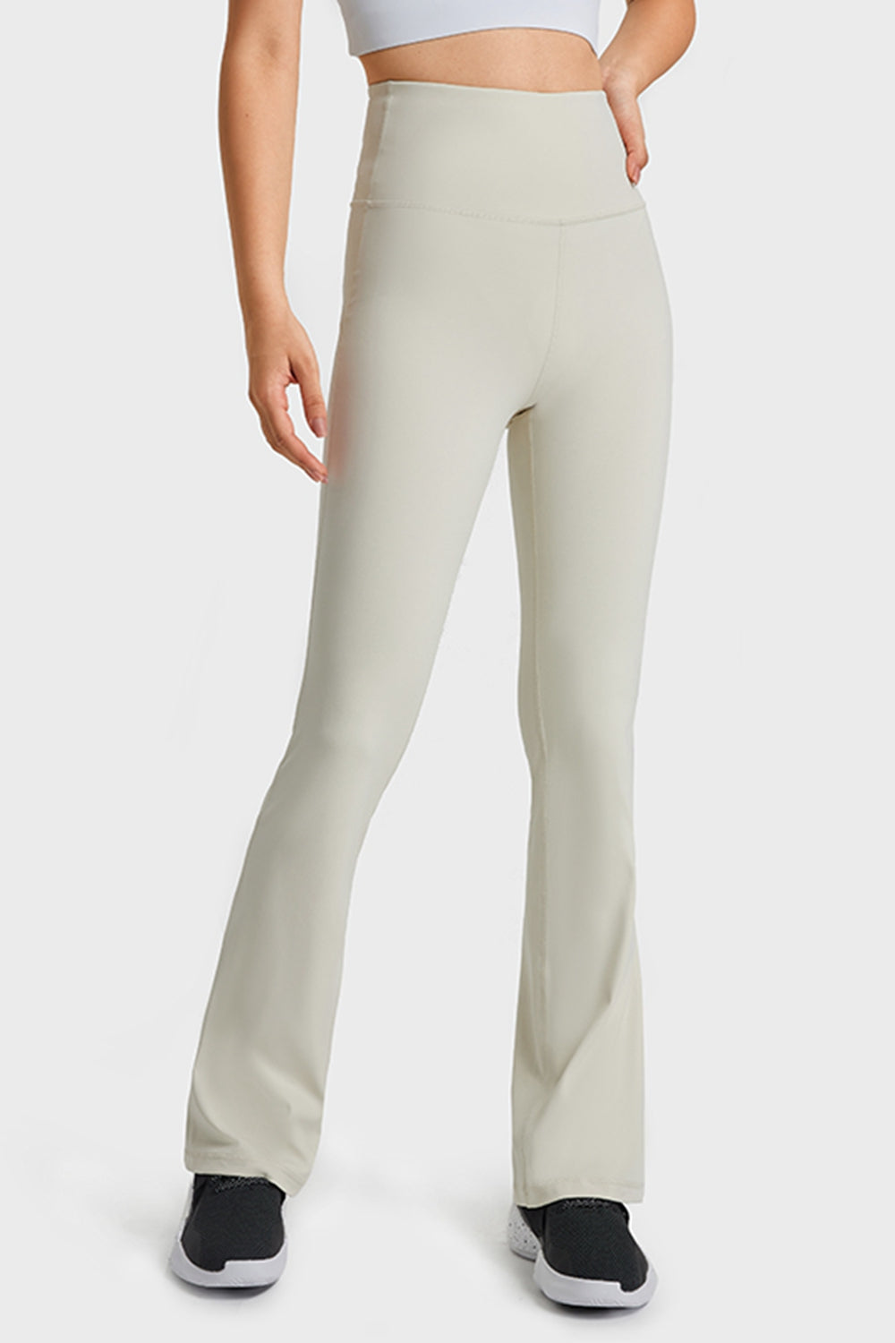 A model wears solid cream elastic-waist flare yoga pants with a high-rise fit, smooth seams, fitted hips and thighs, and long flared legs.