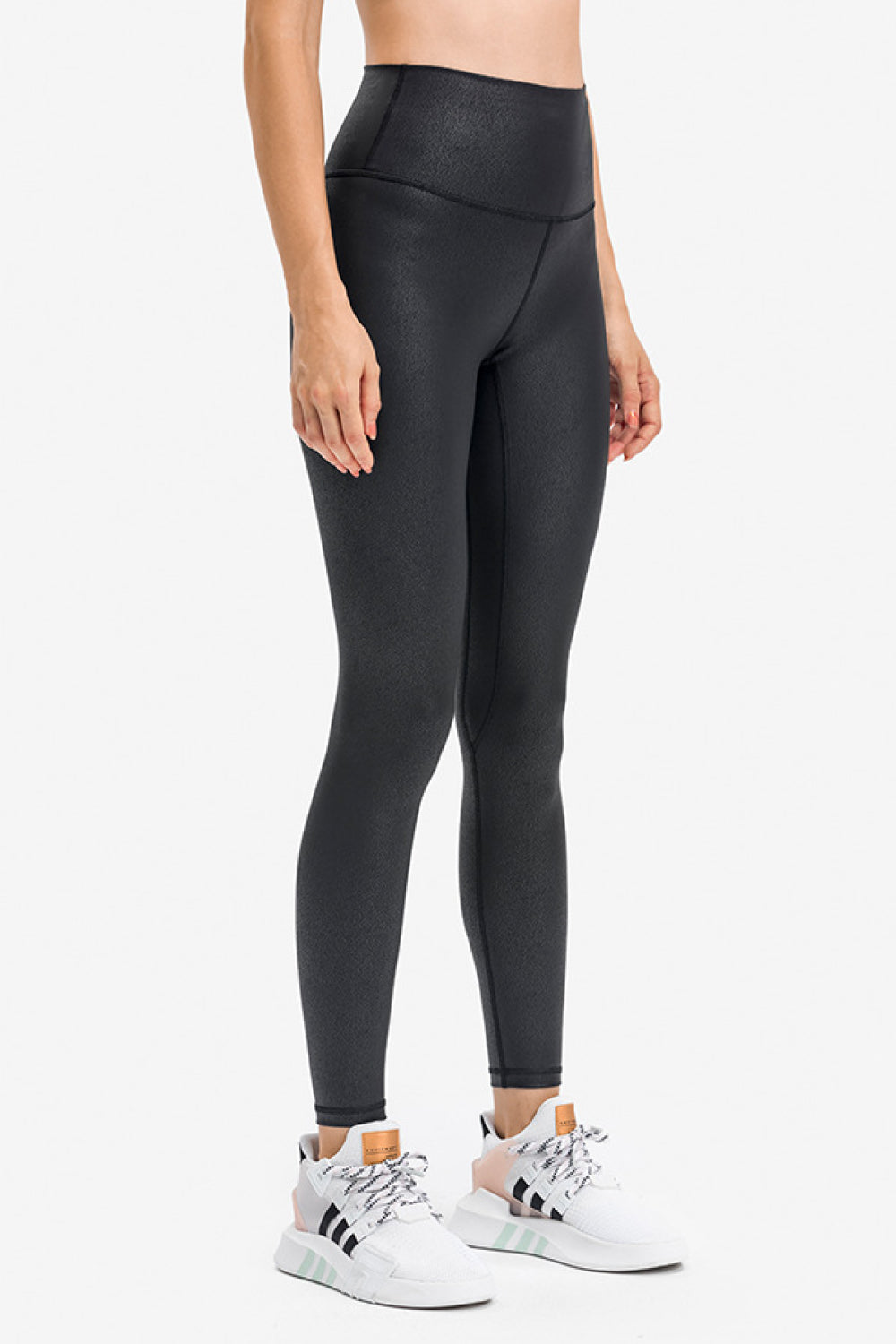 Model stands in black high-rise sports leggings with a slim, ankle-length silhouette, smooth matte fabric, and visible curved waistband and leg seams.