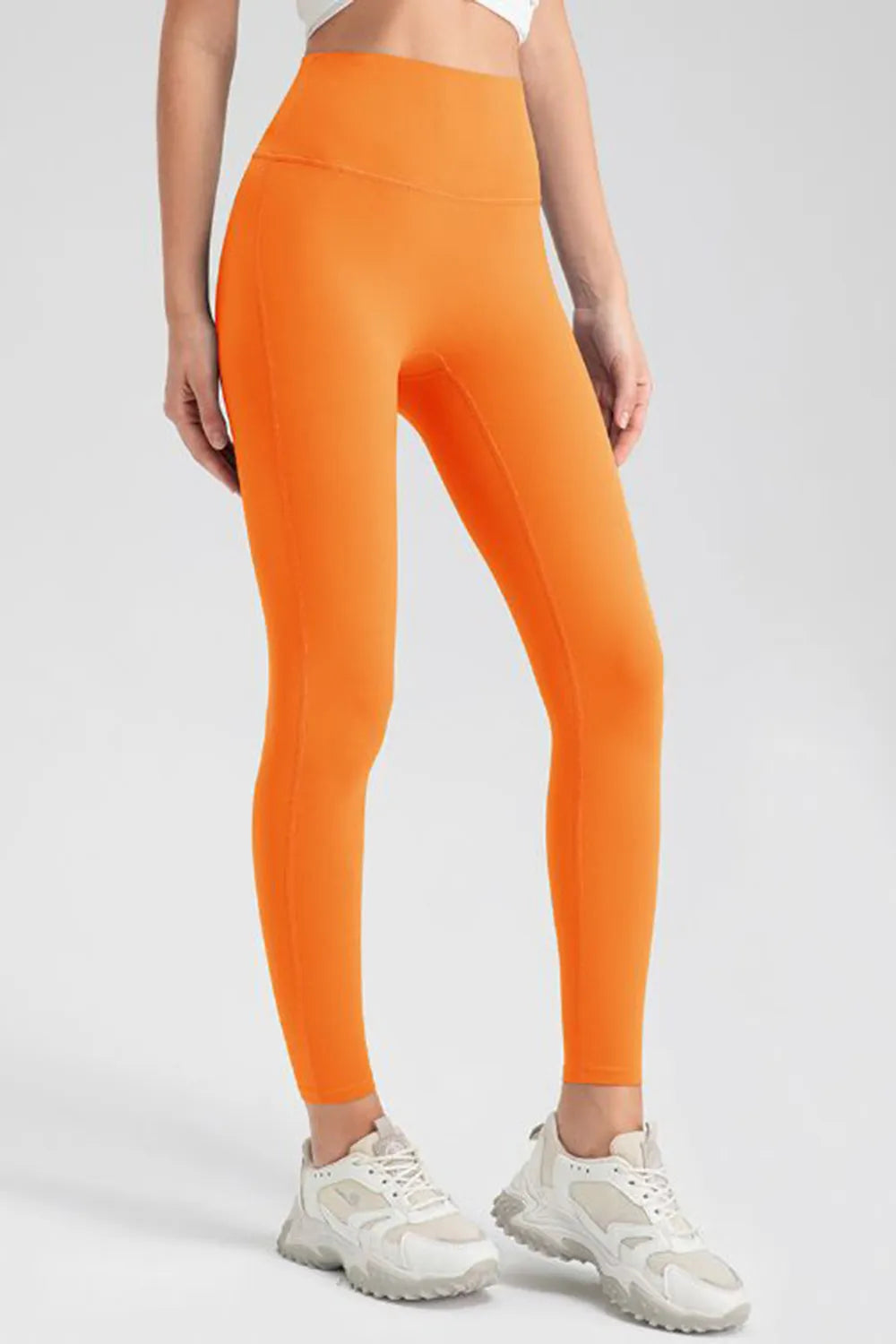Model wears bright orange high-waist skinny active leggings with a smooth, highly stretchy fitted silhouette and visible front seam construction.