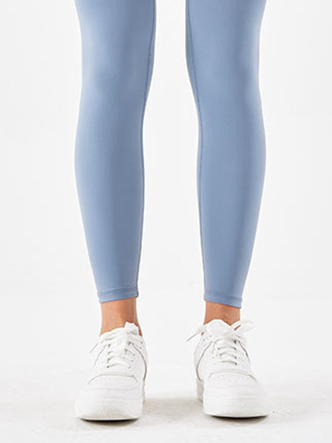 A model stands in light blue sports leggings with a smooth, highly stretchy, close-fitting silhouette that tapers to the ankles.