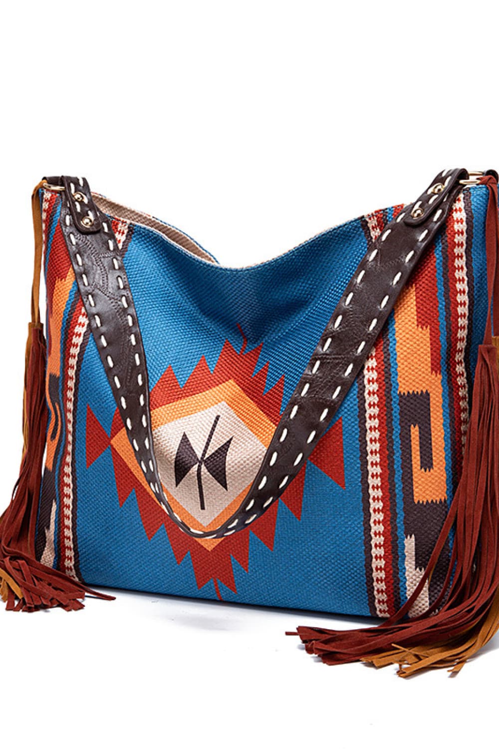 Oversize geometric canvas tote bag in blue with multicolor woven patterns, wide dark straps with contrast stitching, and long fringe trim.