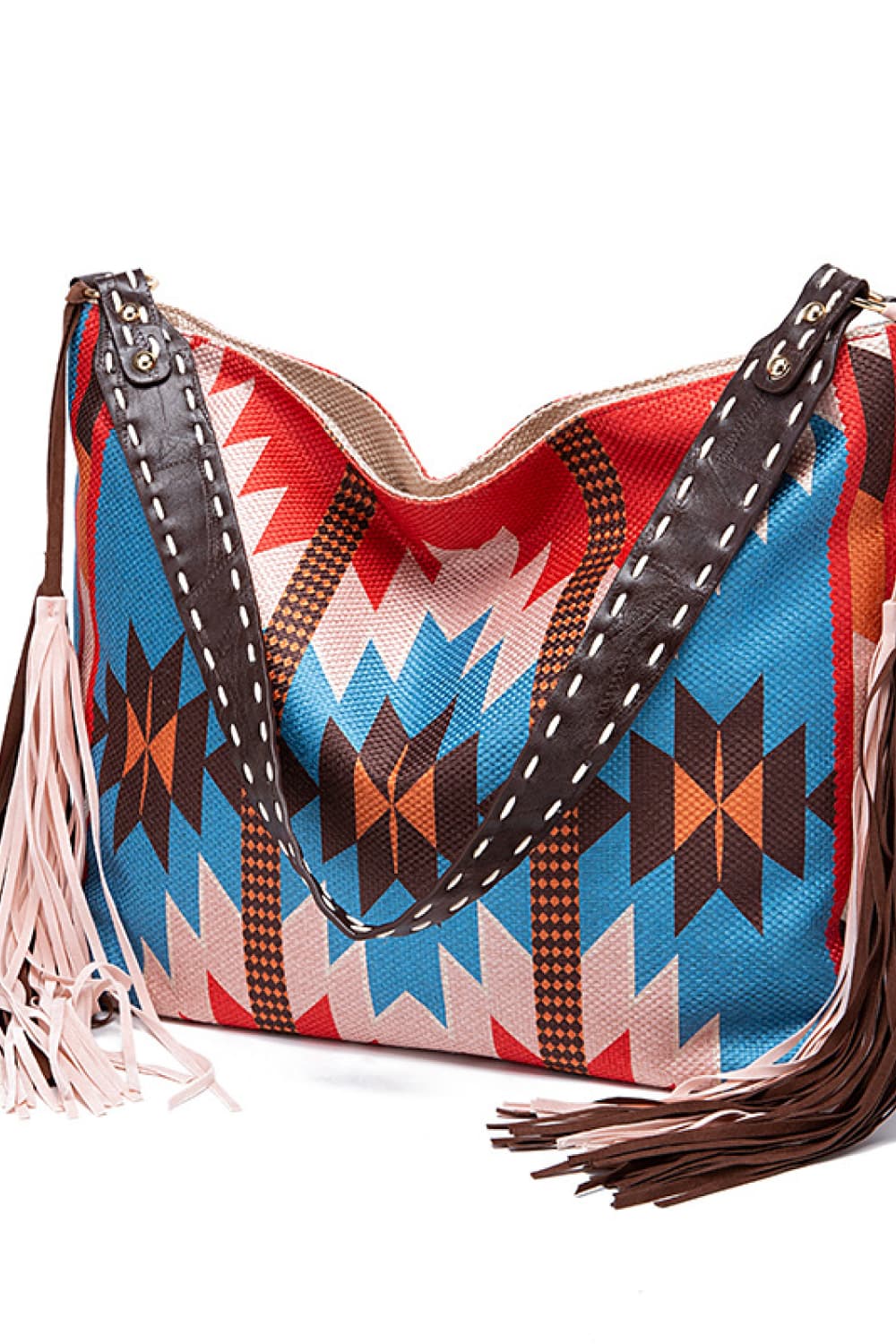 Oversize geometric canvas tote bag in blue, red, pink, orange, and brown, featuring sturdy dark straps, an open top, and long fringe trim.