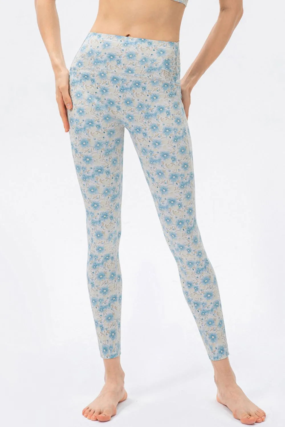A model stands with hands at her hips wearing high-waist skinny leggings in a light blue floral print with a fitted ankle-length silhouette.