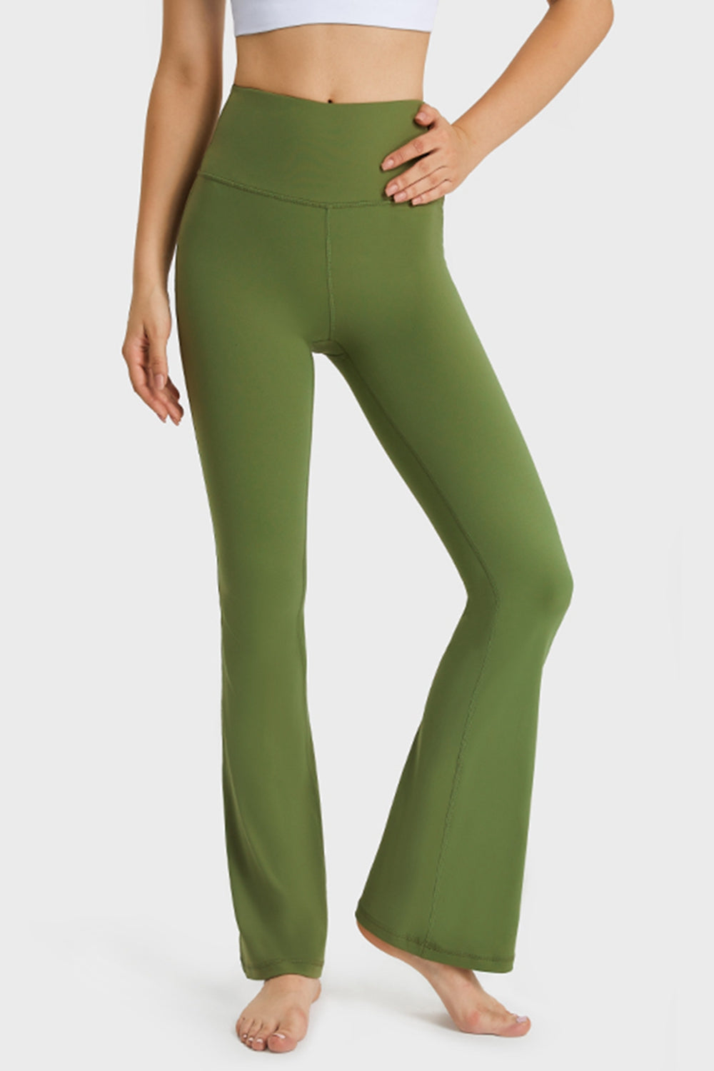 Model wearing olive green elastic-waist flare yoga pants with a wide waistband, fitted hips, visible seams, and long flared legs, posing with one knee bent.