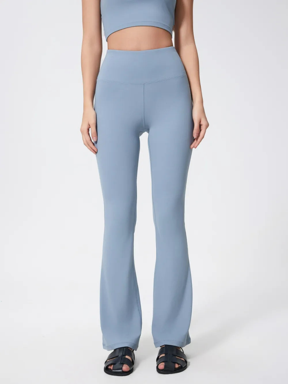 Model standing in light blue high-waist active pants with a fitted stretch silhouette, seamed waistband, and gently flared full-length legs.