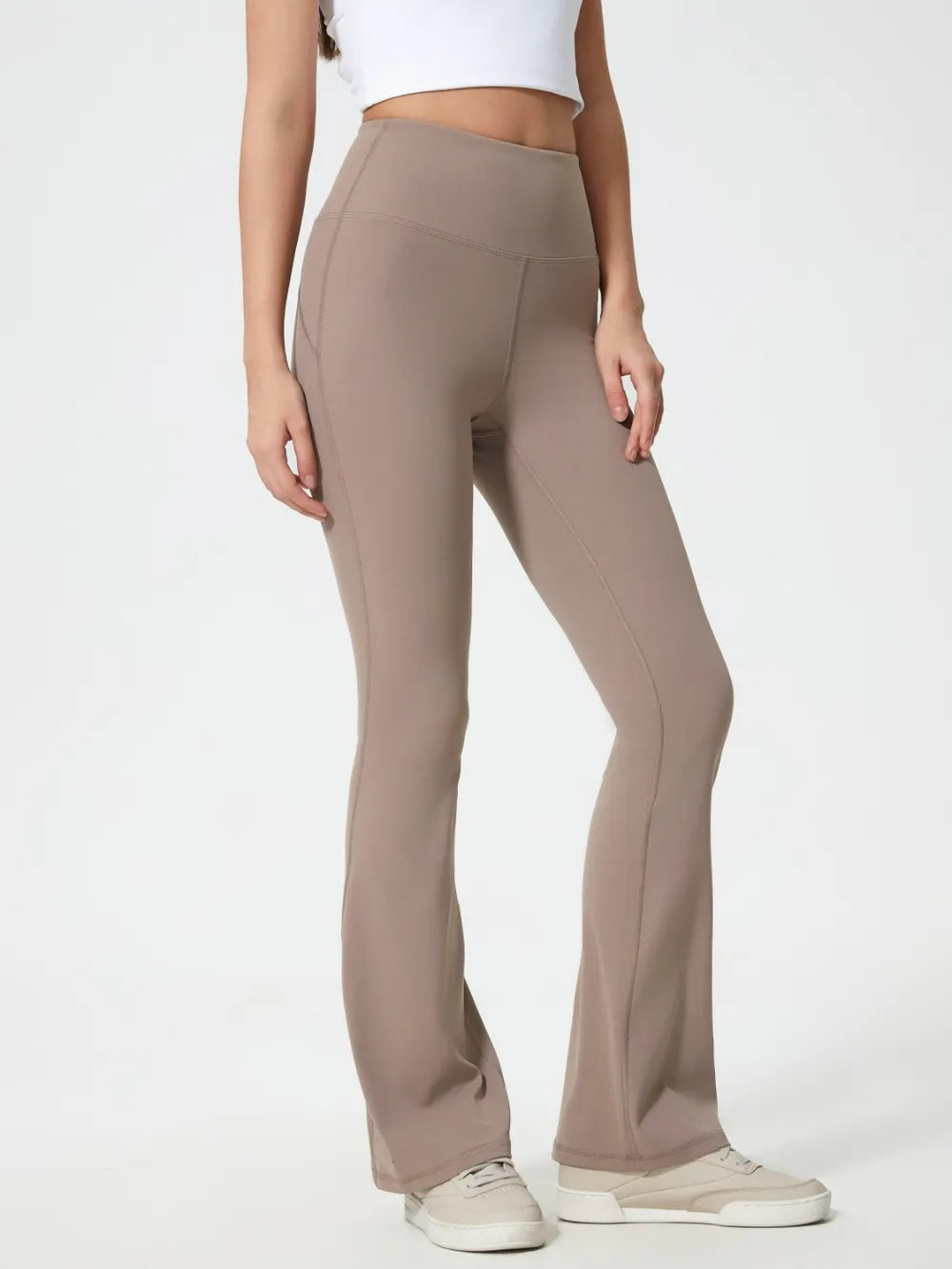 Model stands with hands at her sides wearing taupe high waist active pants with a fitted silhouette, flared legs, and visible seam construction.