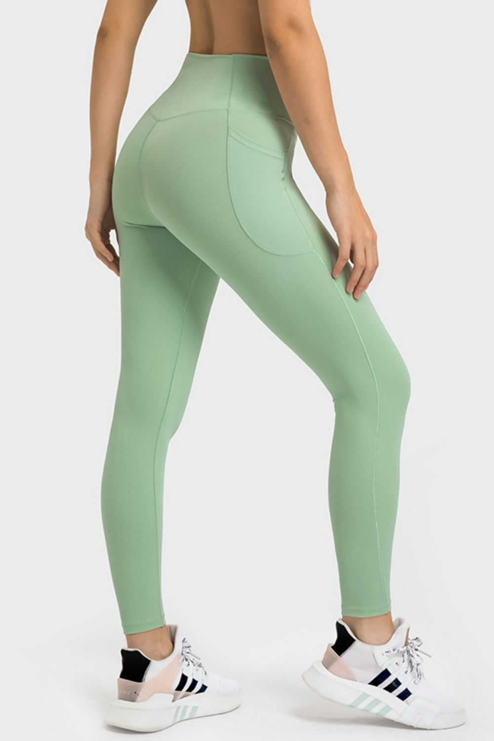 Model shown from behind in mint green V-waist yoga leggings with side pockets, a close-fitting silhouette, and curved seam detailing in a bent-leg pose.