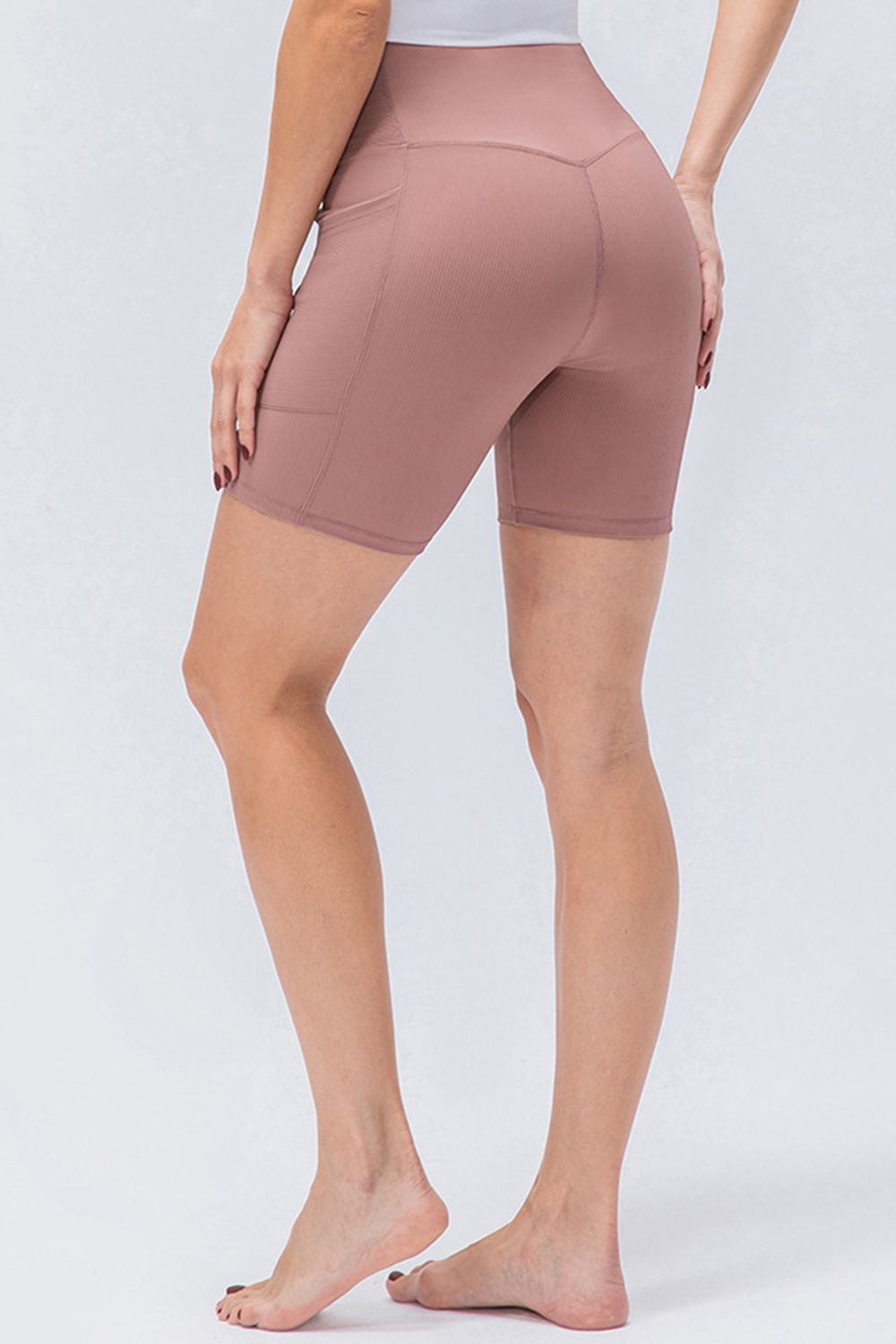 A model stands in a rear three-quarter pose wearing solid mauve slim-fit sports shorts with a V-waistband, stretch silhouette, and visible seam detailing.