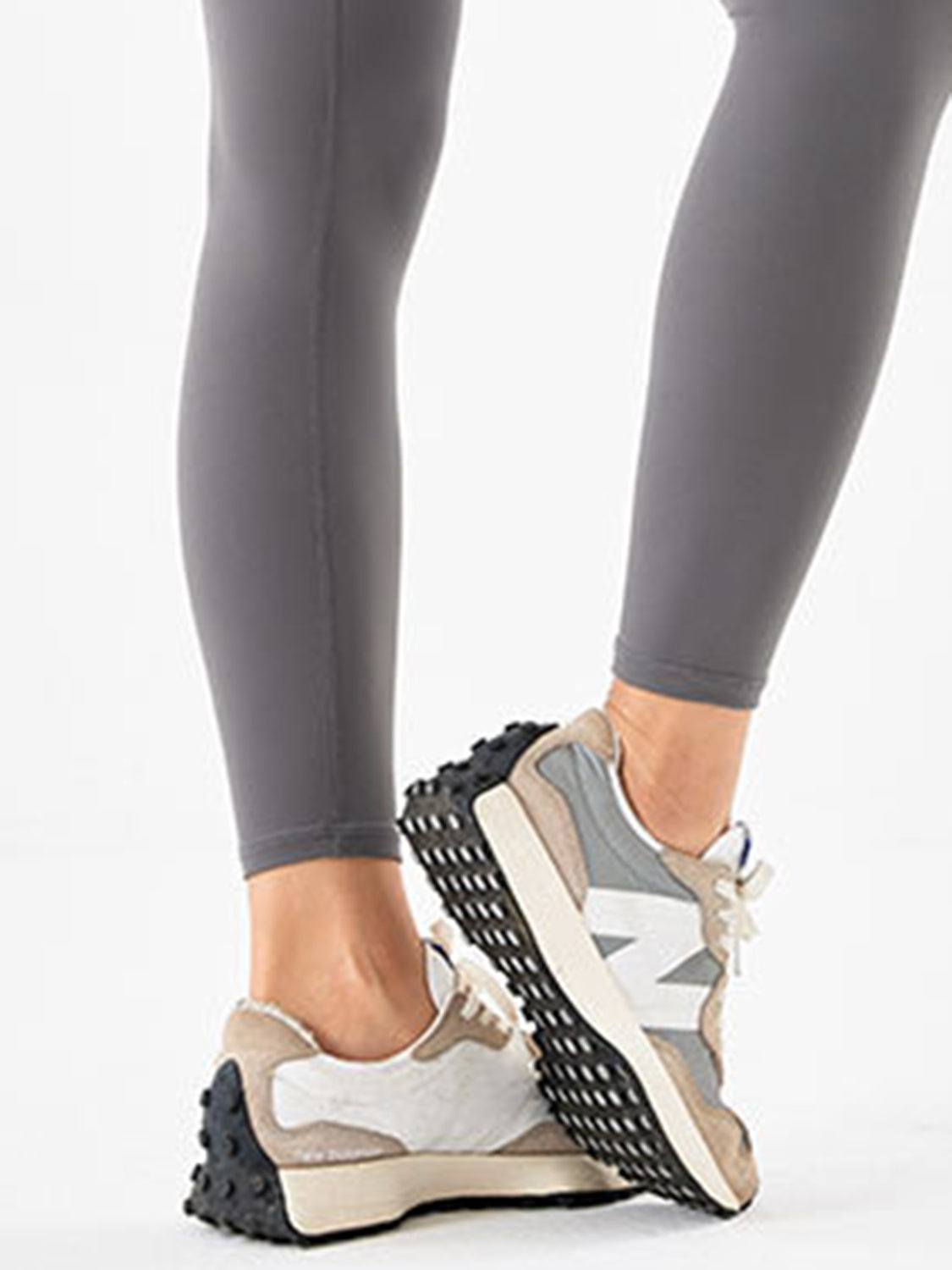 Visible model wears dark gray sports leggings with a fitted full-length silhouette, ankle-length hems, and subtle vertical seams in a crossed-leg pose.