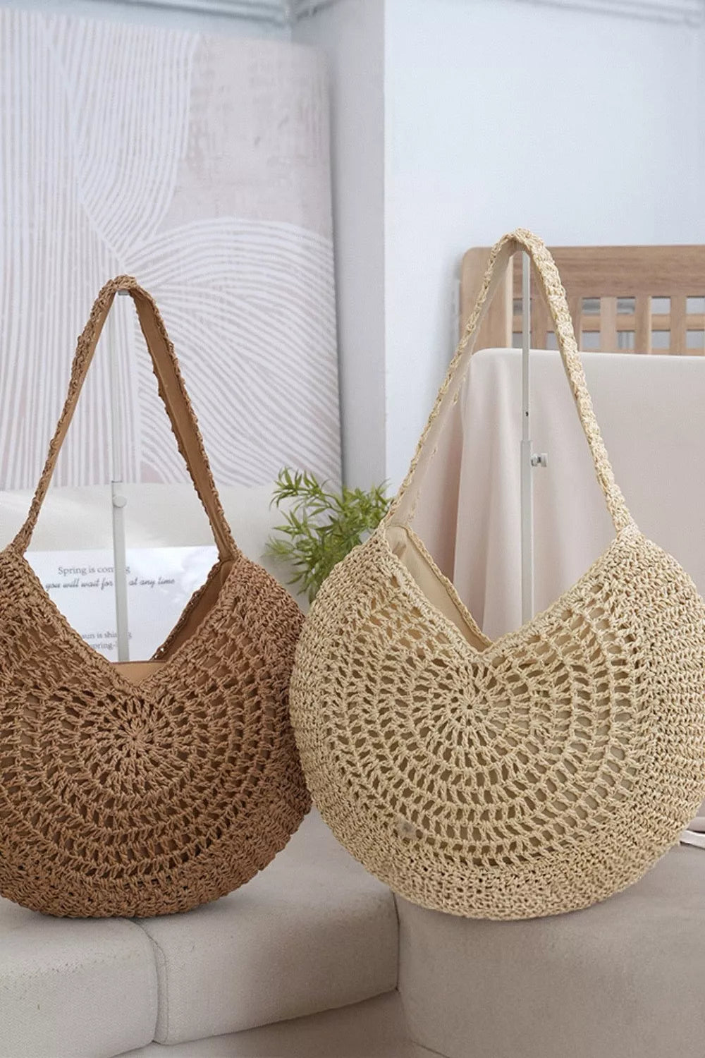 A medium natural-beige round woven shoulder bag features an openwork crochet texture, circular motif, curved silhouette, and long braided strap.