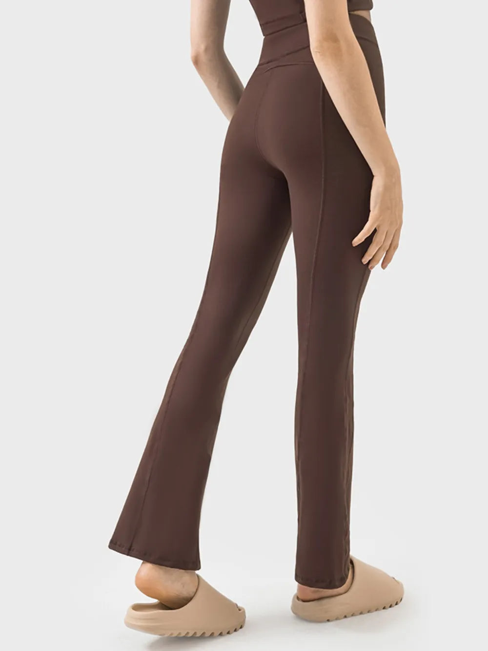 Model shown from the back wears brown high-waisted active pants with a fitted silhouette, subtle stretch, full-length legs, and flared hems.