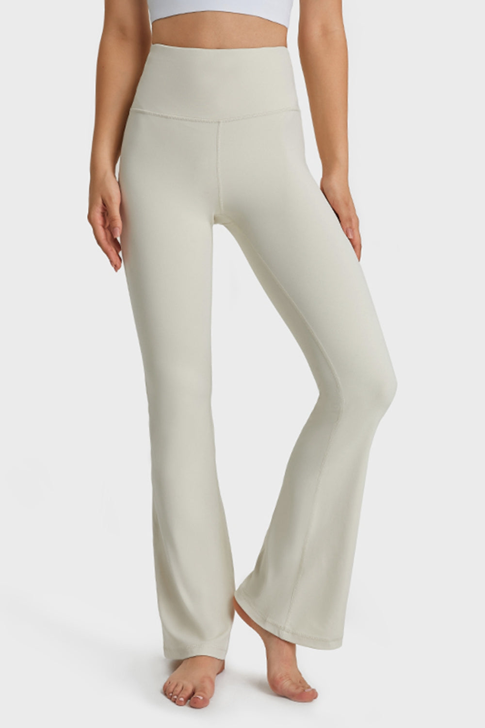 Model poses in cream elastic-waist flare yoga pants with a high-rise waistband, fitted hips and thighs, long flared legs, and visible seam construction.