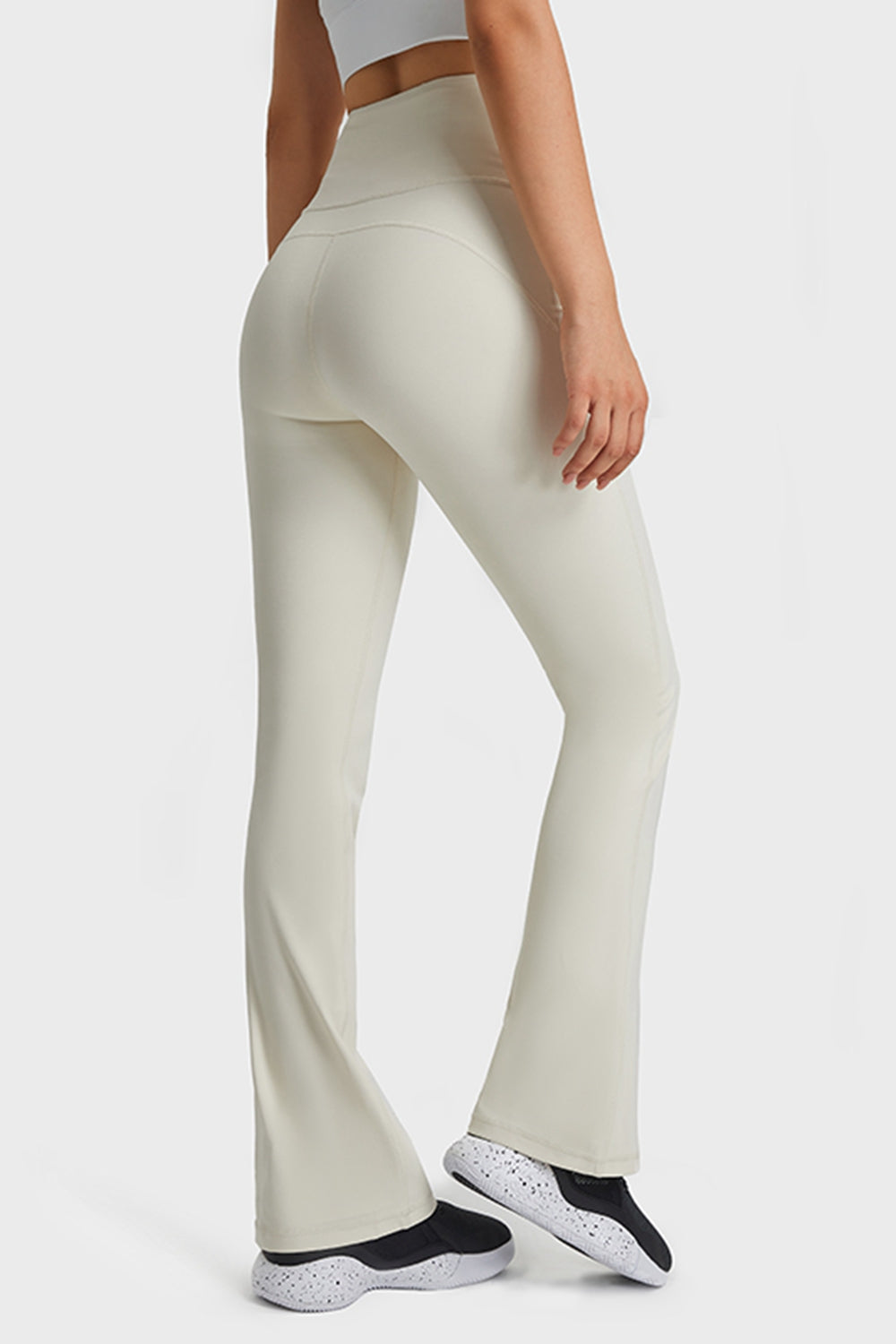 Model shown from behind wearing solid ivory elastic-waist flare yoga pants, fitted through the hips and thighs with a long, stretchy silhouette and flared hems.