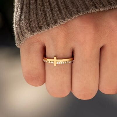 A hand displays a slim 18K gold-plated 925 sterling silver cross ring with a row of sparkling zircon stones and a polished band.