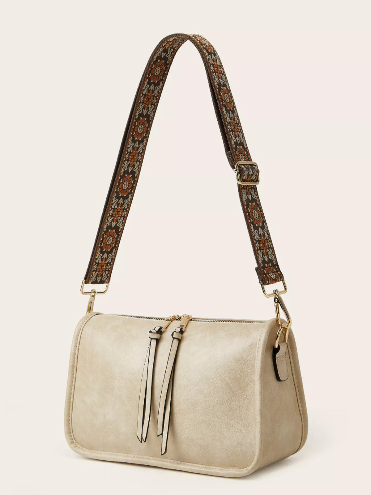 Small cream PU leather crossbody bag with a vintage patterned brown strap, rounded rectangular silhouette, top zipper, and front tie details.