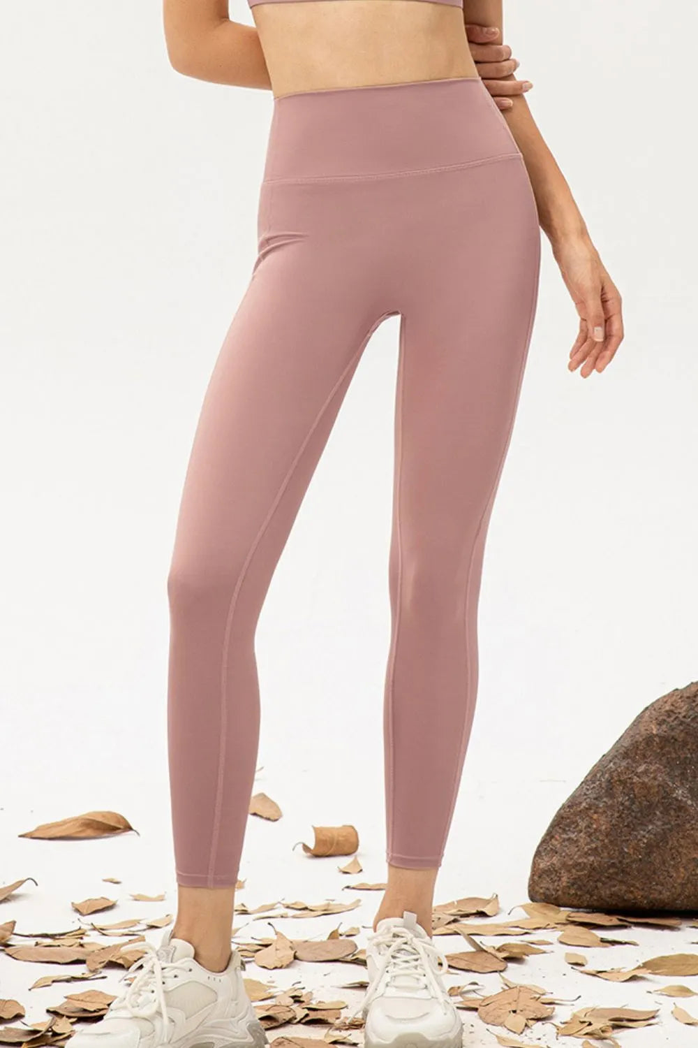 Model wearing mauve high-waist skinny active pants with a smooth fitted silhouette, wide waistband, and visible leg seams, standing with one hand at her waist.