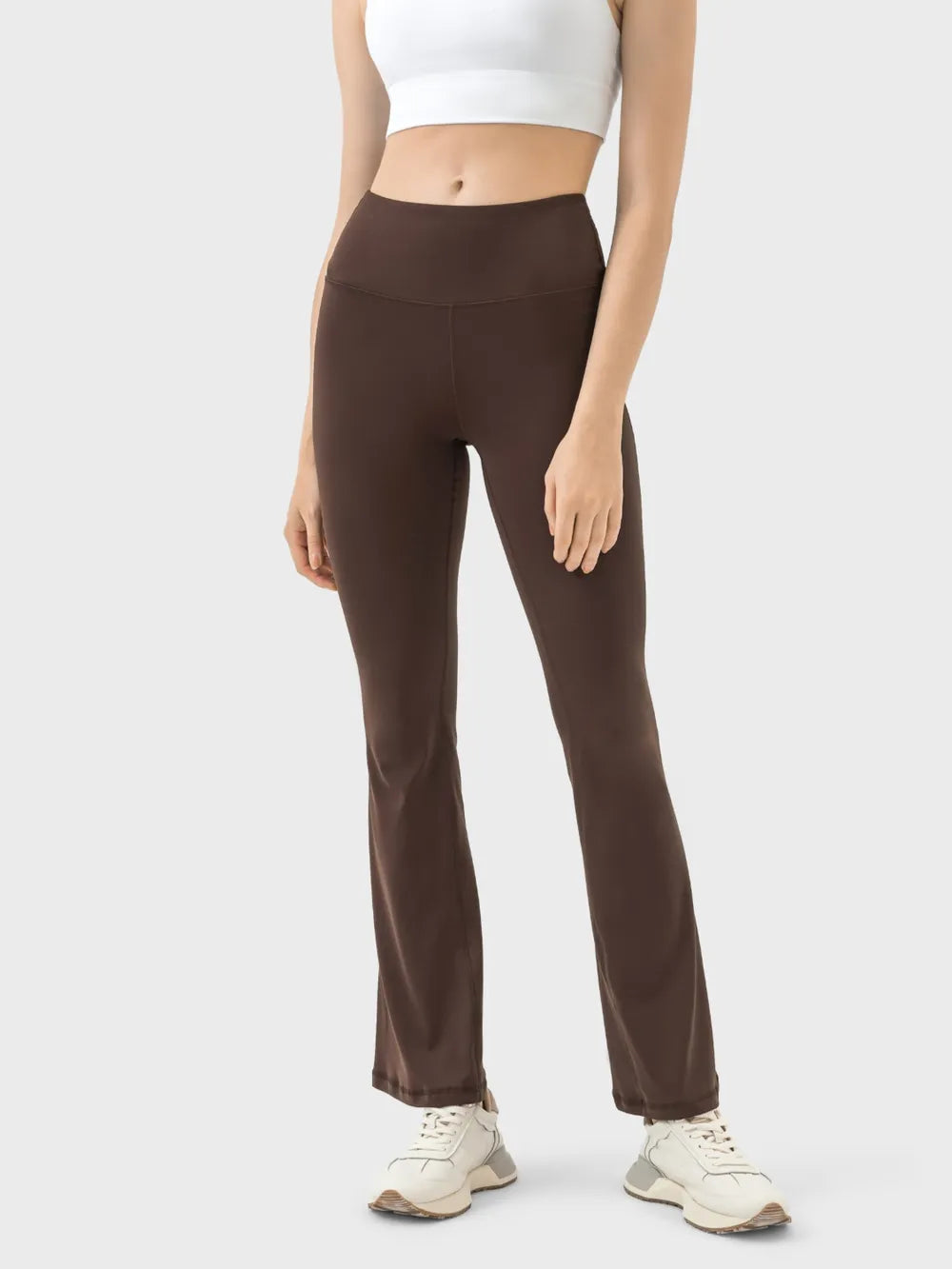 Model wears brown high-waist active pants with a smooth, stretchy, fitted silhouette, wide contoured waistband, straight legs, and visible seam construction.