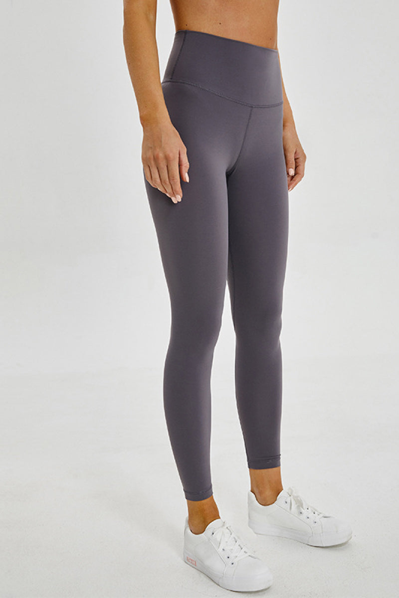 Model stands with hands at her sides wearing charcoal-gray sports leggings with a wide seamless waistband, fitted full-length silhouette, and ankle hems.