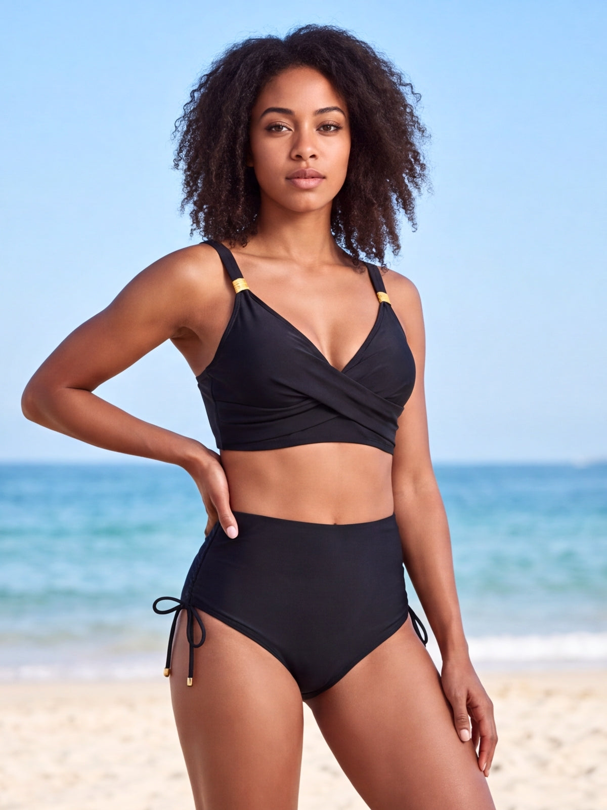 A model poses with one hand on her hip wearing a black crisscross bikini top and high-waisted bottoms with side drawstring ties.