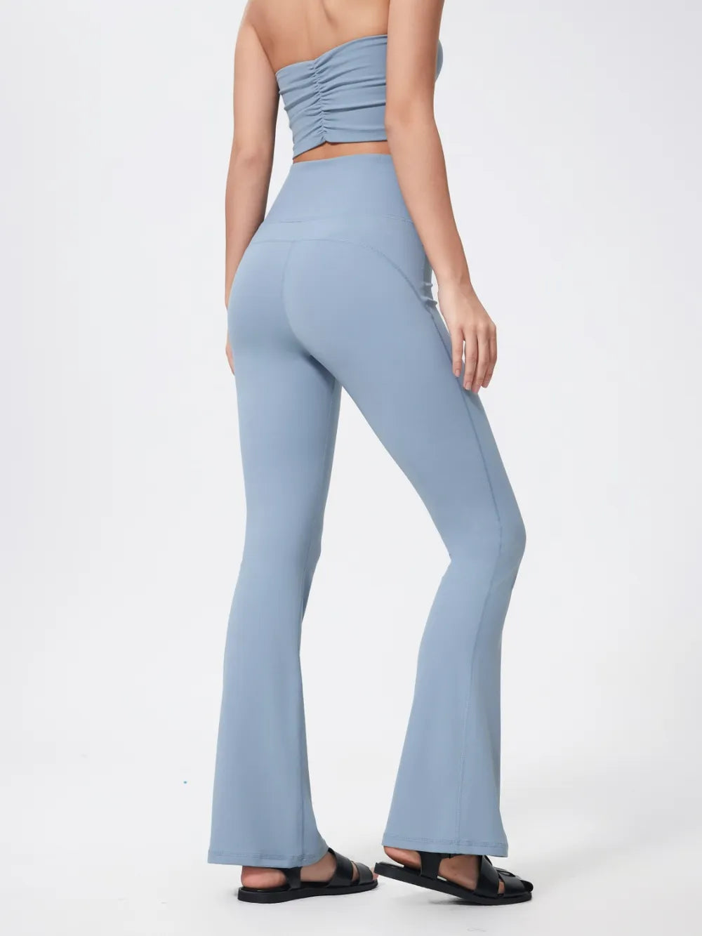 Model wears light blue high waist active pants with a sleek, stretchy fit, flared legs, and visible seam construction while posing in black sandals.
