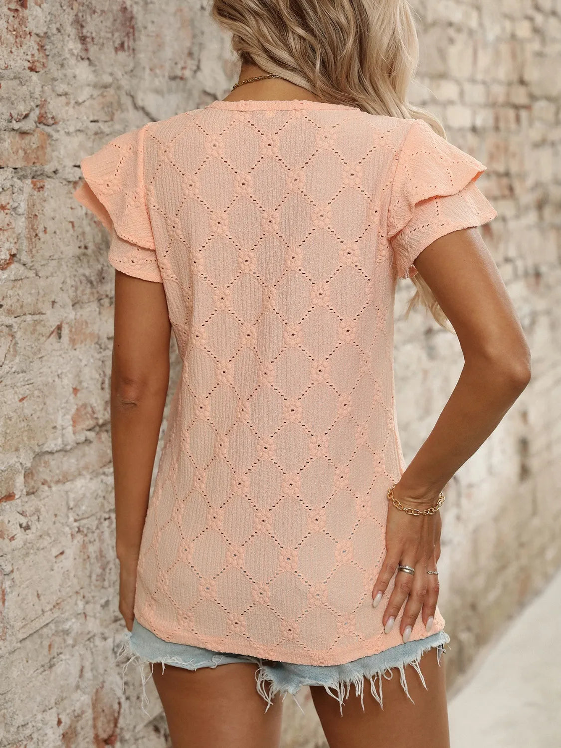 Eyelet V-neck ruffled cap sleeve top with decorative buttons and lace.