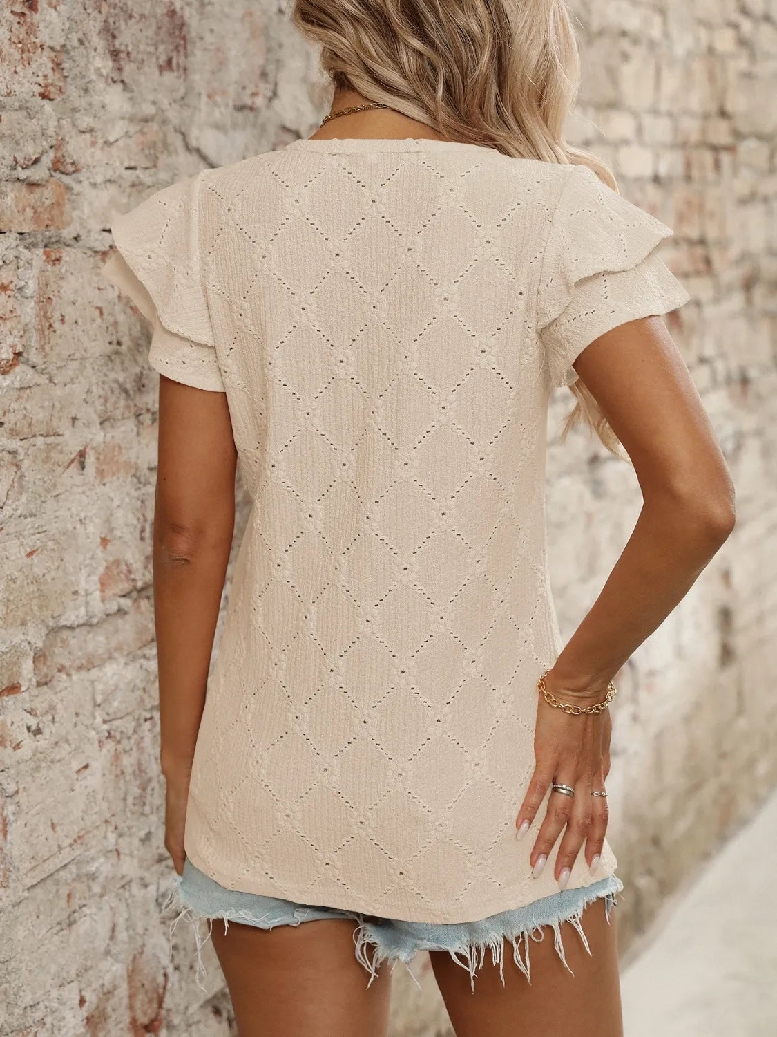 Eyelet V-neck ruffled cap sleeve top with decorative buttons and lace.