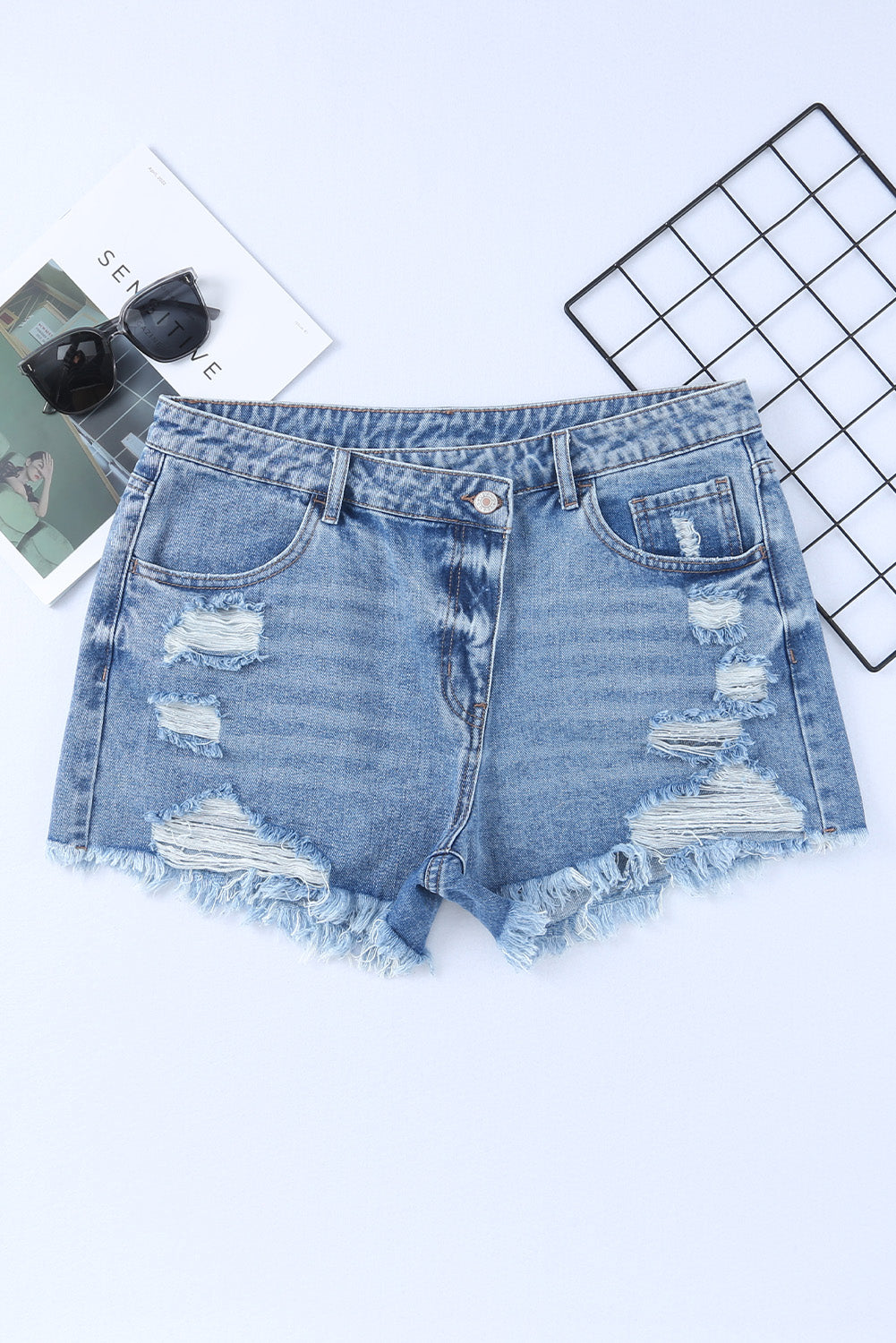 High rise crossover waist denim shorts with buttons, distressed details, and raw hem.
