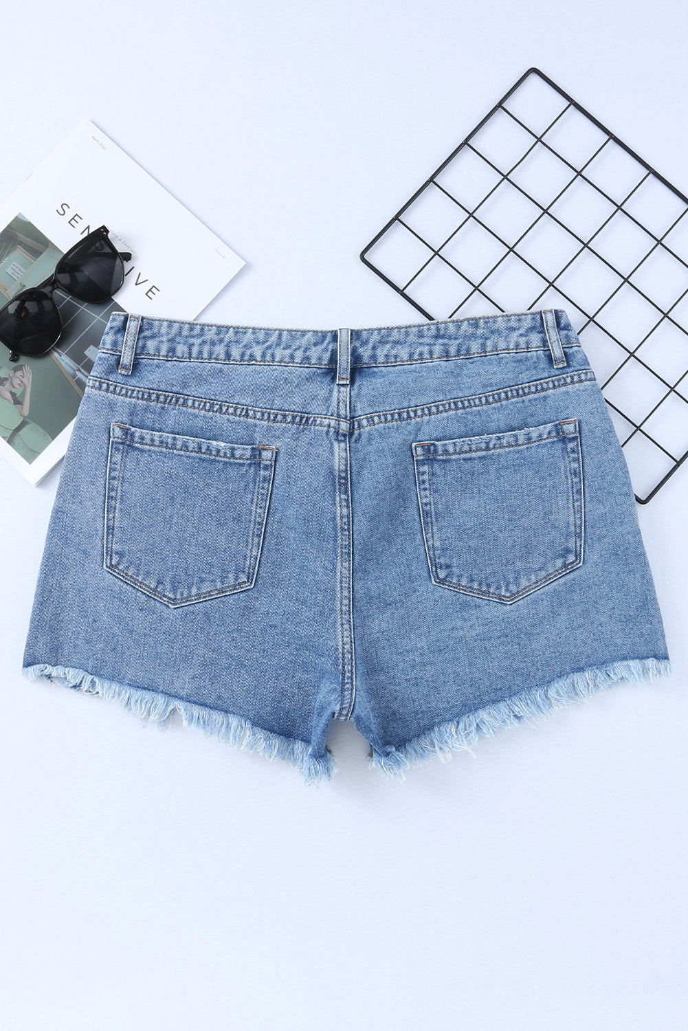 High rise crossover waist denim shorts with buttons, distressed details, and raw hem.