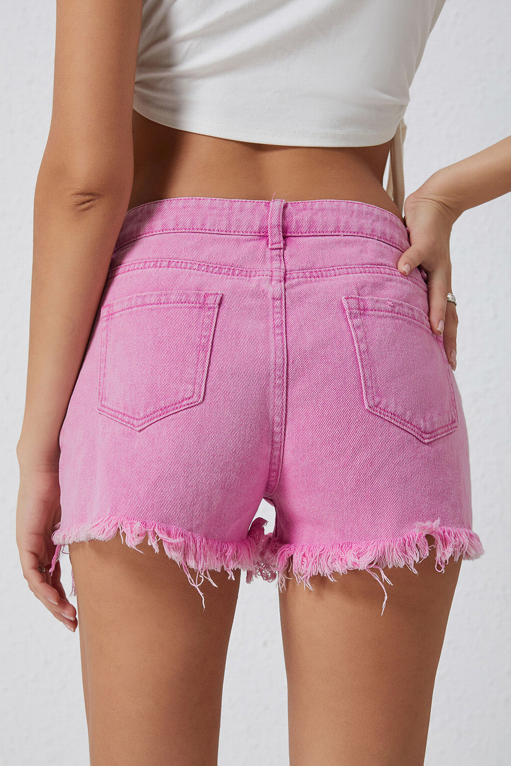 High rise crossover waist denim shorts with buttons, distressed details, and raw hem.